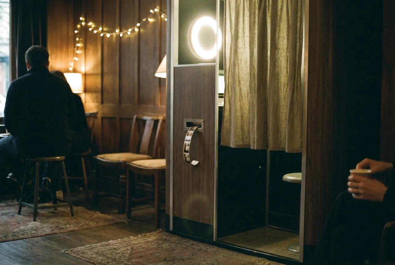 A photo booth switched on in a quiet, softly lit room, its ring light glowing and a fresh print sliding out