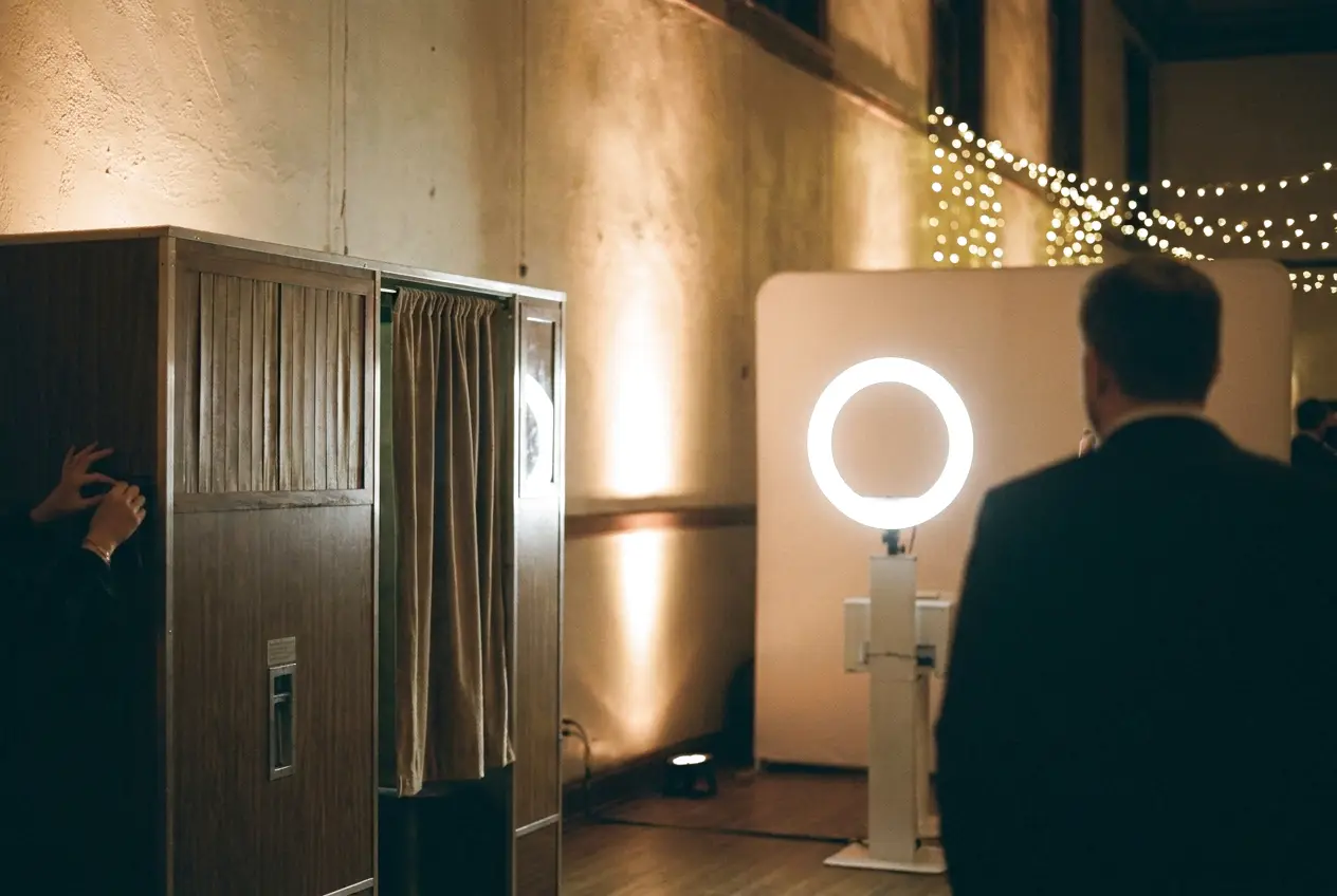 Two different photo booths side by side in an empty ballroom under soft uplighting